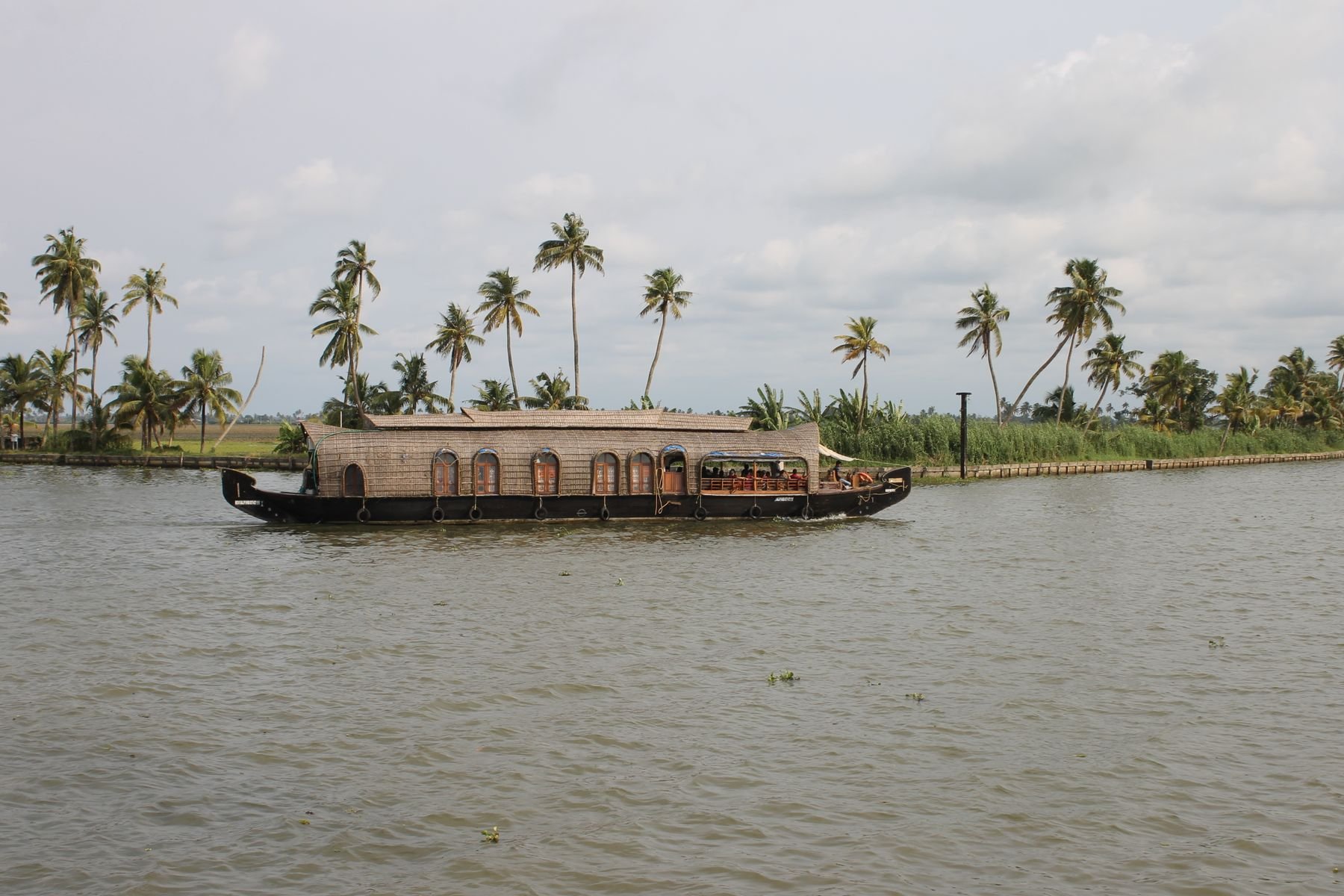 A houseboat moves through palm-lined Kerala backwaters